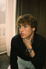 Man in a black shirt, hand at his chin, wearing the watch