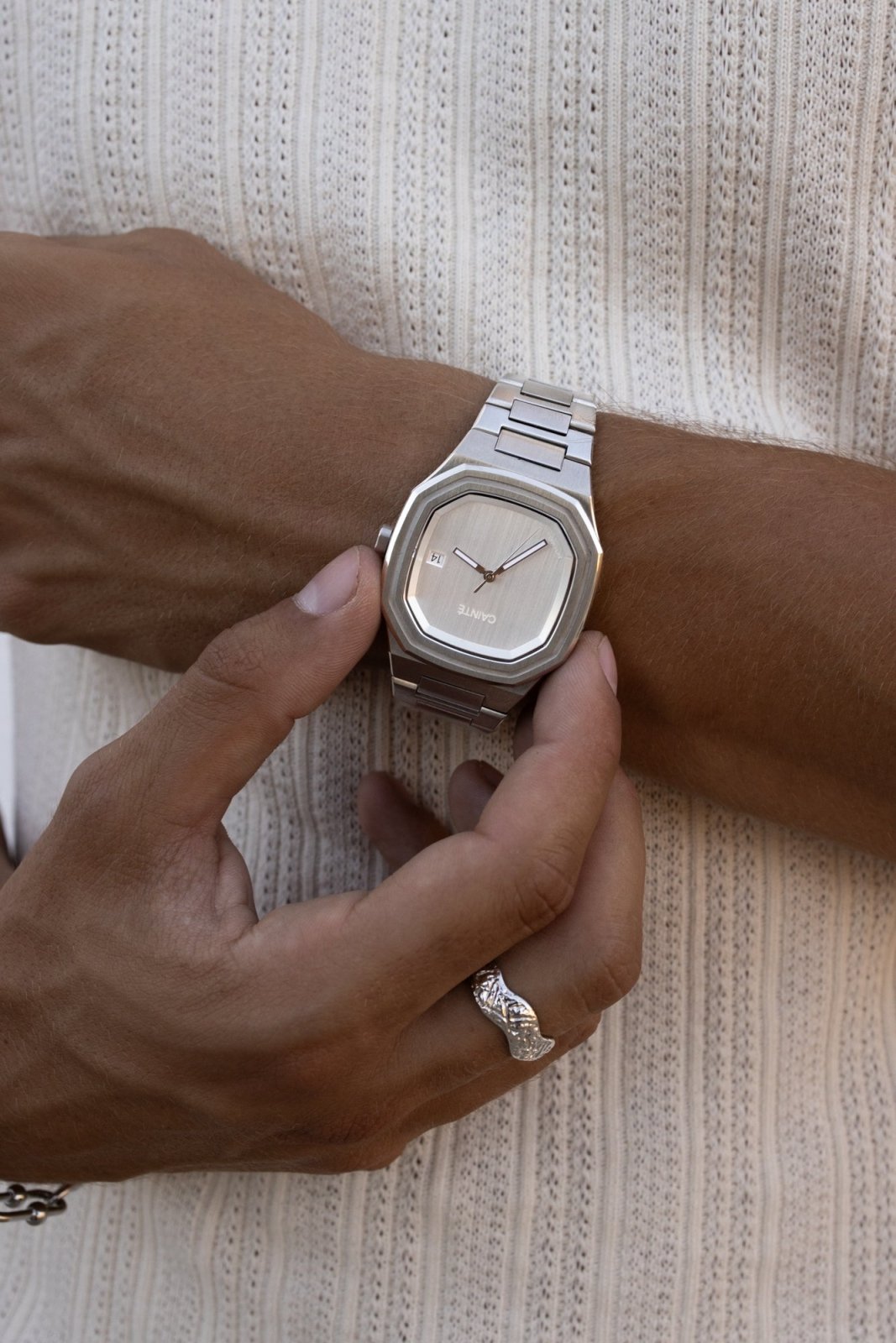Fingers on the watch against a ribbed knit top