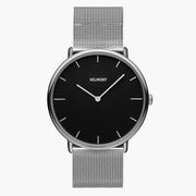 A black dial framed by a slim silver-tone case, set on a silver-tone mesh strap.