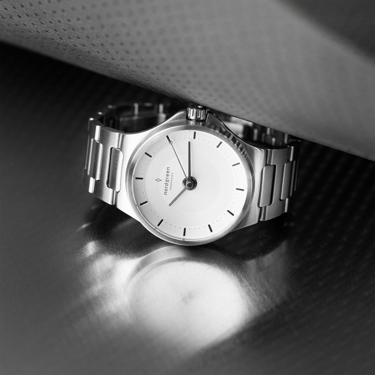 Silver-tone watch resting in a dark setting under a dramatic light.