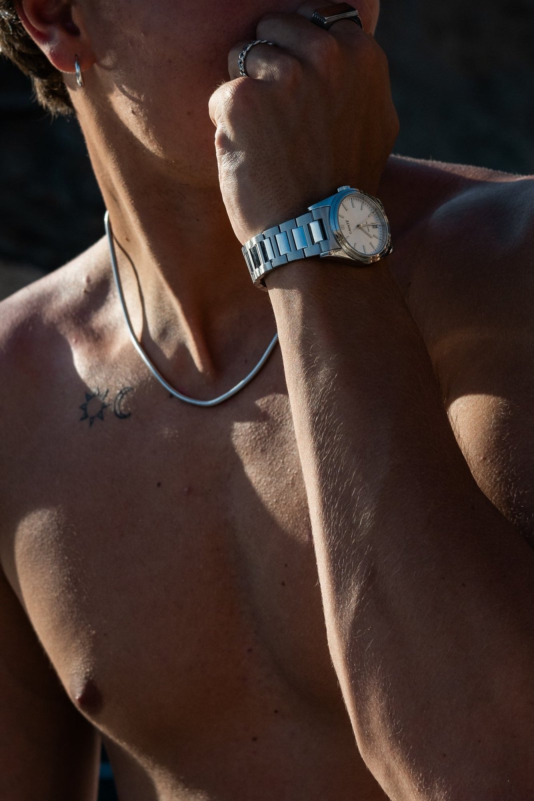 Hand raised to the face wearing the round watch