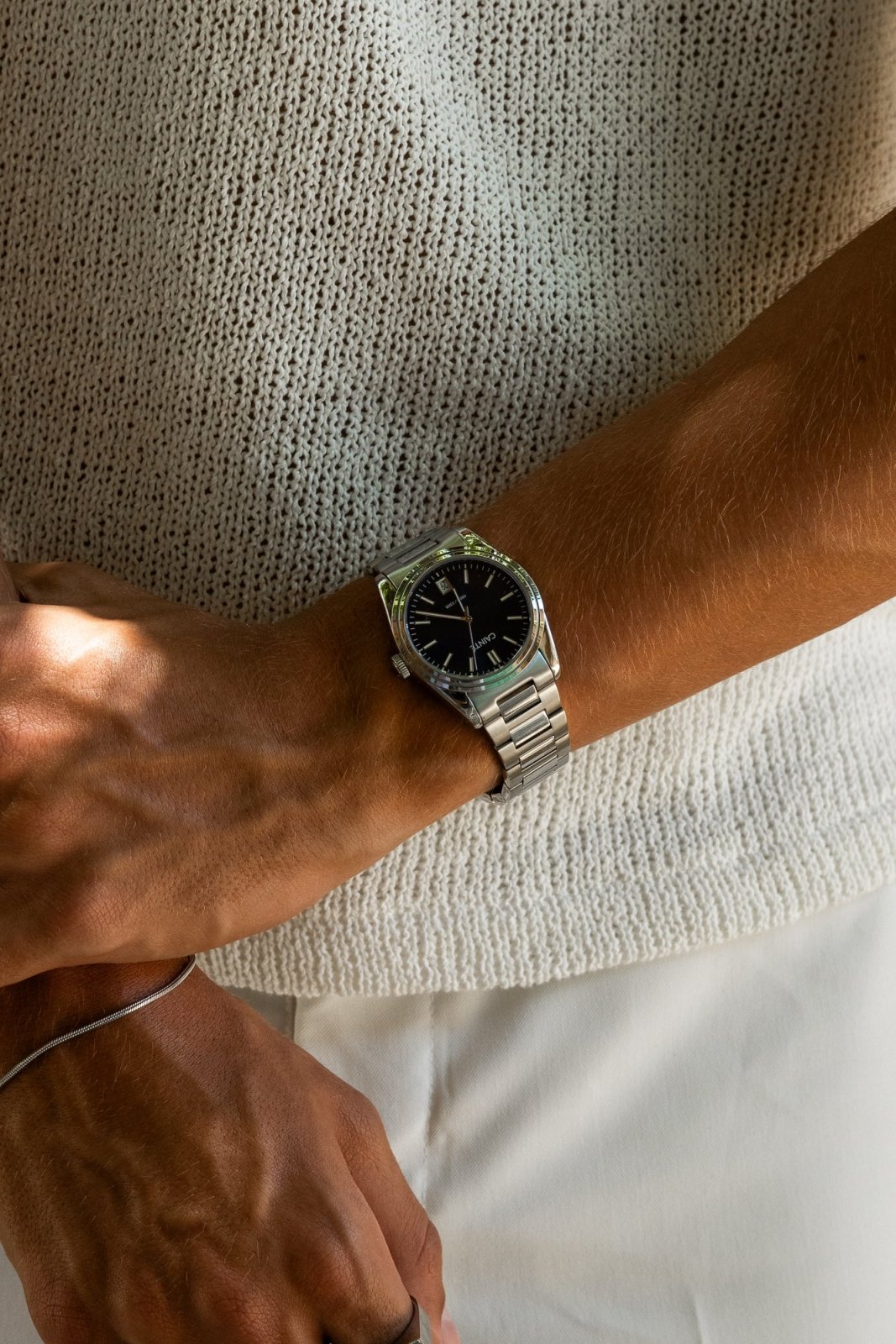 Arms crossed over a knit top, round watch on the wrist