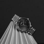 The watch resting on a pleated gray pedestal against a dark backdrop.