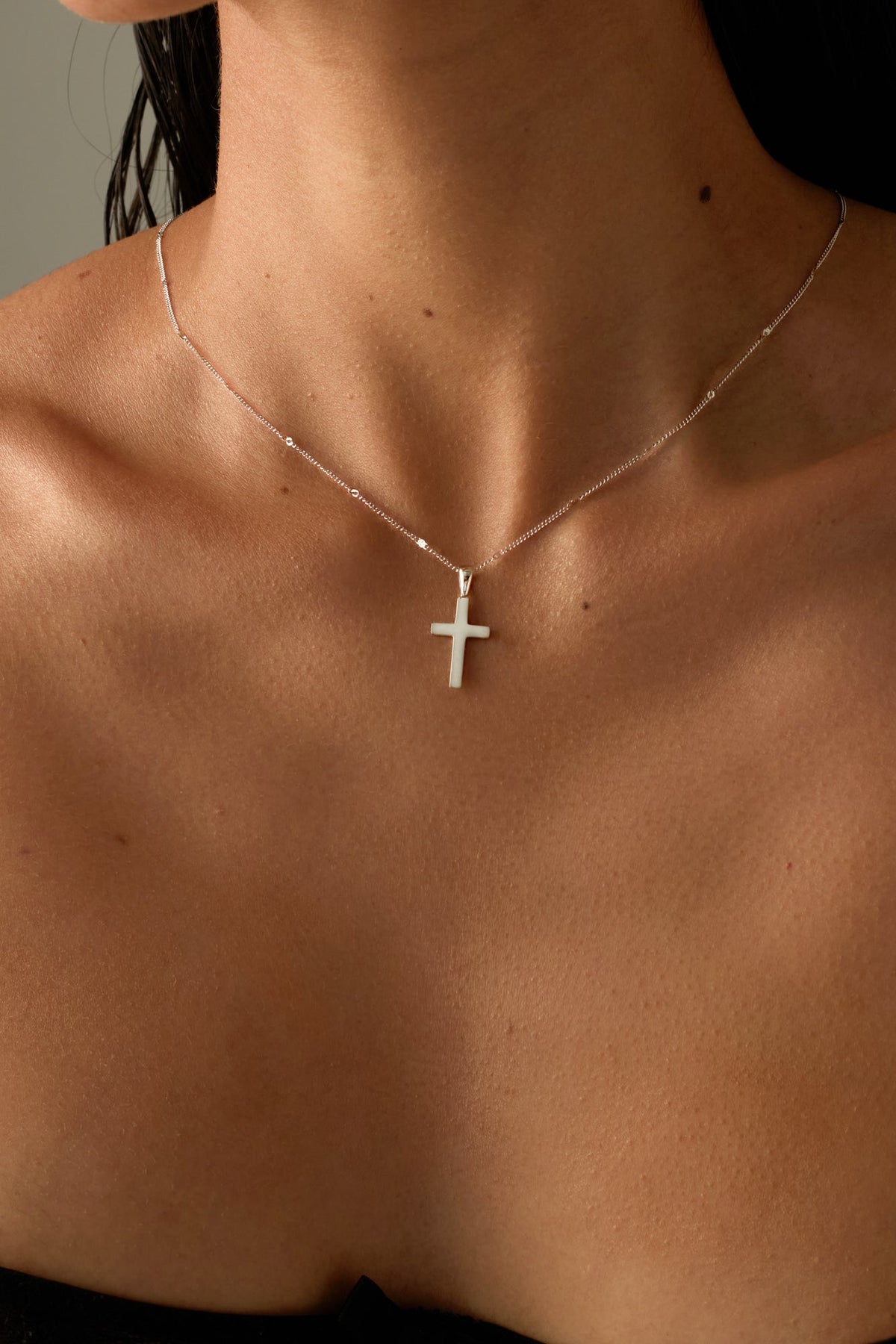 Cross pendant necklace worn at the collarbone, close-up