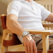 Man in a white polo seated in a wooden armchair wearing the watch.