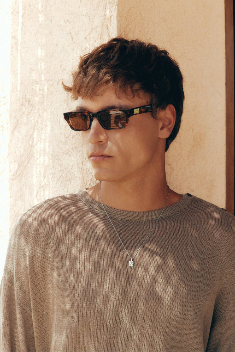 Man wearing the tortoise sunglasses against a sunny wall