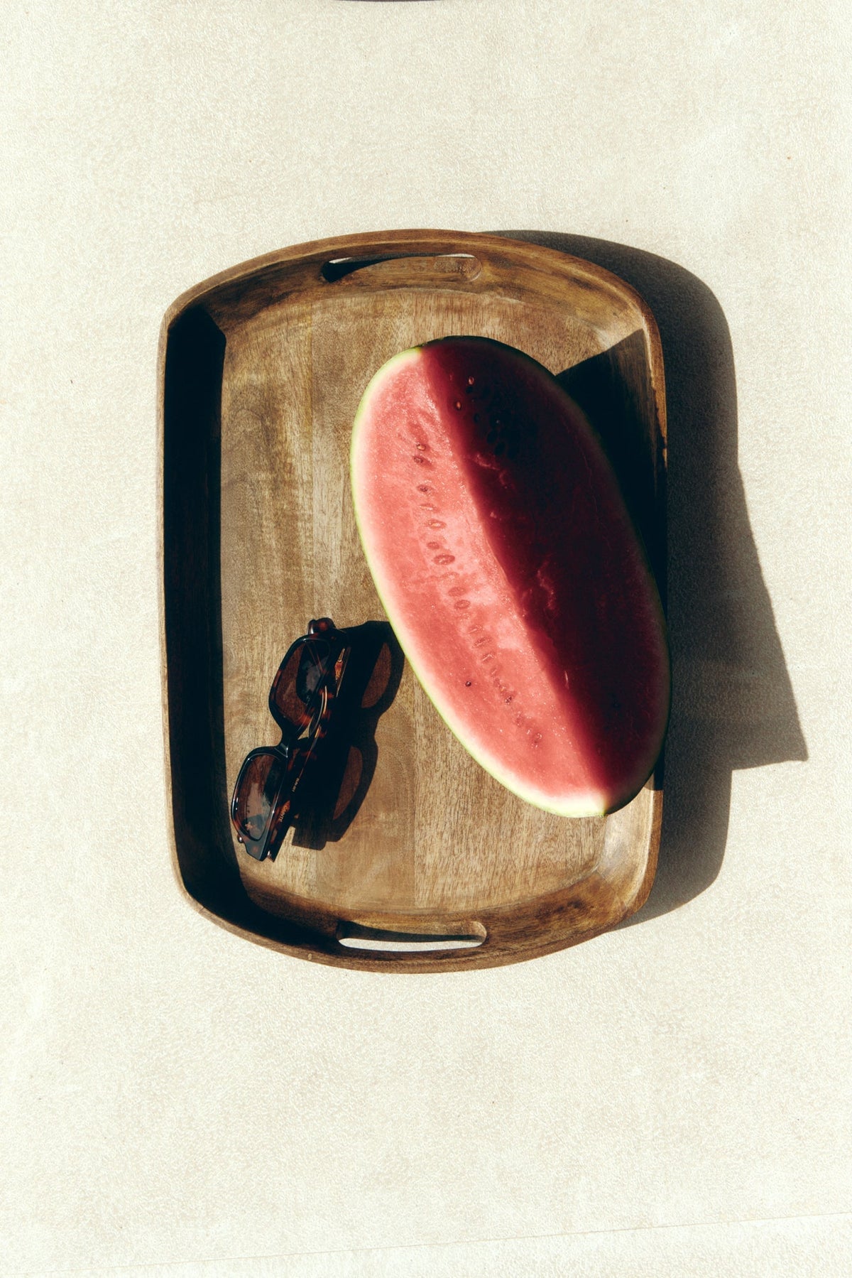Tortoise sunglasses on a wooden tray next to watermelon