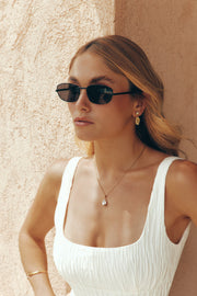 Woman against a sandy wall wearing the thin sunglasses