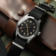 Field watch on a nylon strap resting on a brown leather case