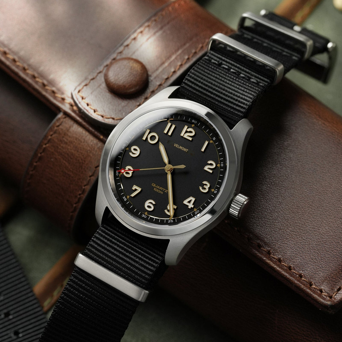 Field watch on a nylon strap resting on a brown leather case